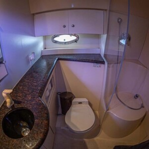 Compact bathroom with a small sink, toilet, corner shower, and black countertop. Small window above the counter.