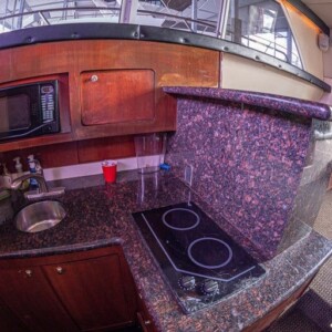 Boat kitchen with a red cup on the counter, microwave, sink, and stove. Granite surfaces and wooden cabinets dominate the space.